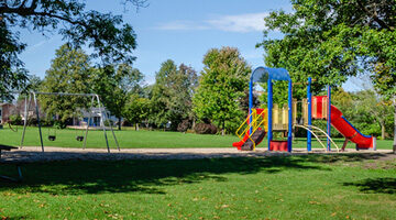 Neighborhood park and playground area on a summer day with shade and a blue sky,